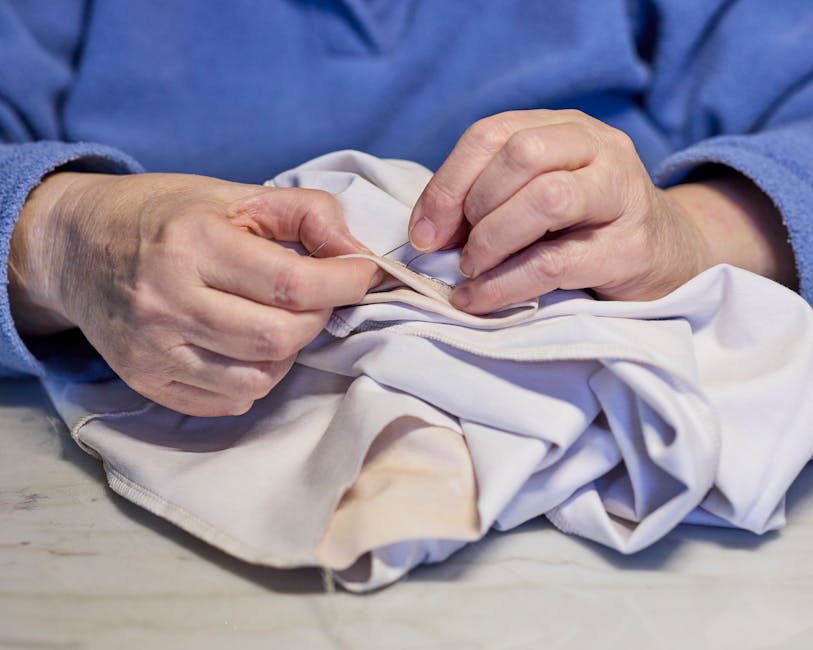 person mending torn seam on a shirt with needle and thread